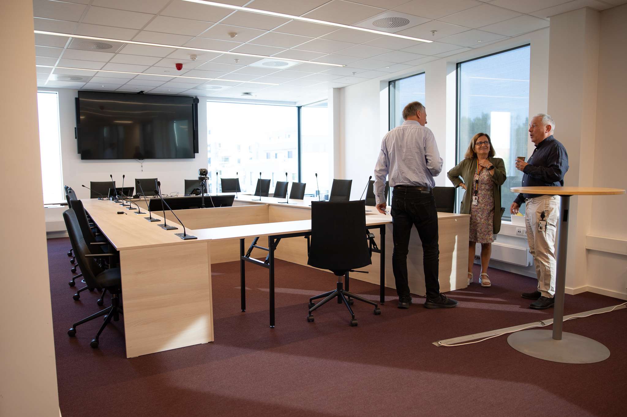 To menn og en kvinne snakker sammen i et stort, moderne møterom. Foto.