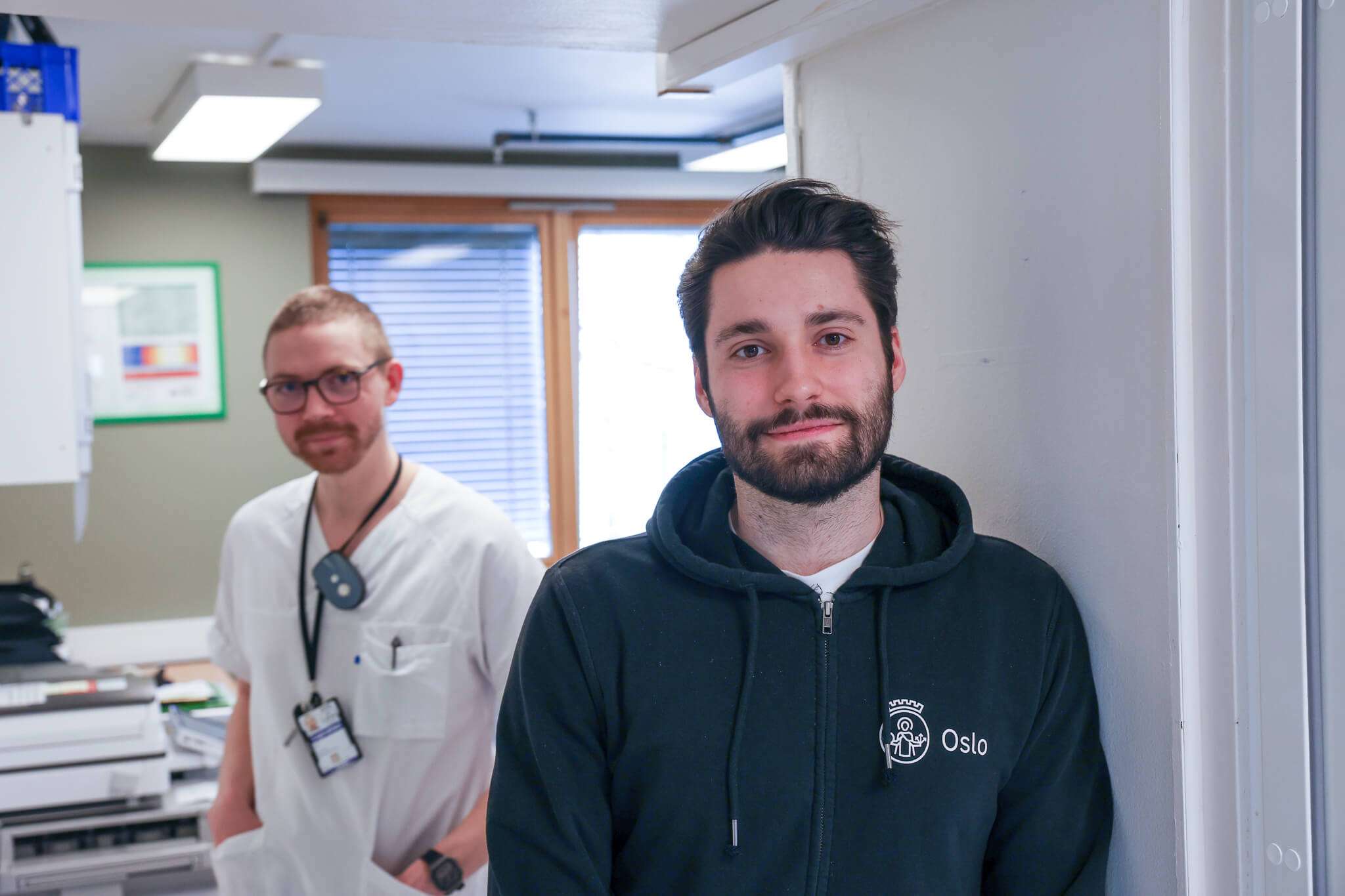 En sykepleier og en utvikler ser i kamera på legevakta, foto