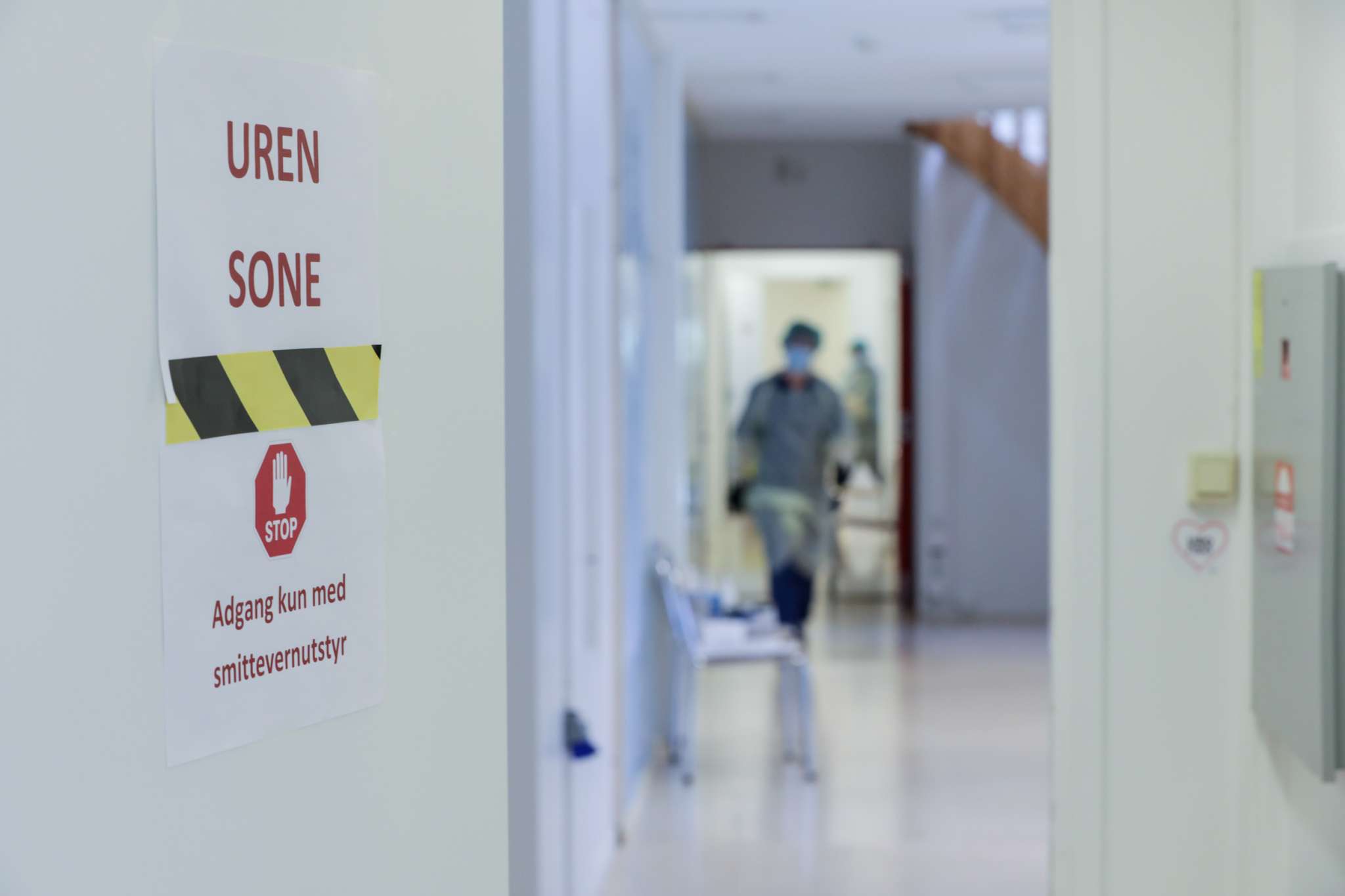 Helsearbeider i smittevernutstyr i en trappeoppgang, innenfor en dør med skiltet "Uren sone - adgang kun med smittevernutstyr"