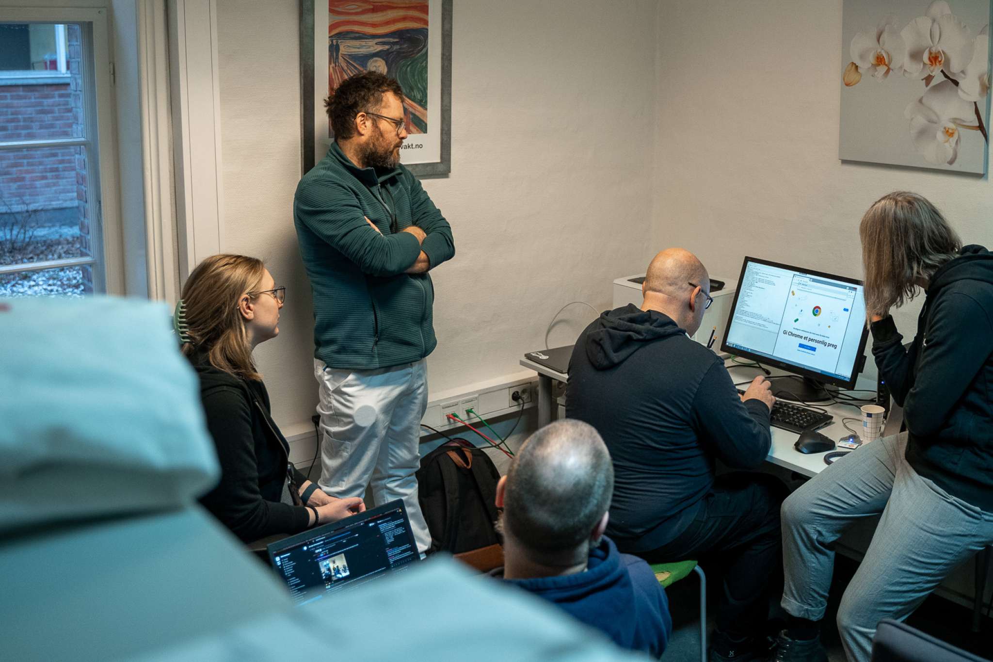 En lege ser på en gruppe utviklere som programmerer på en datamaskin. Foto.