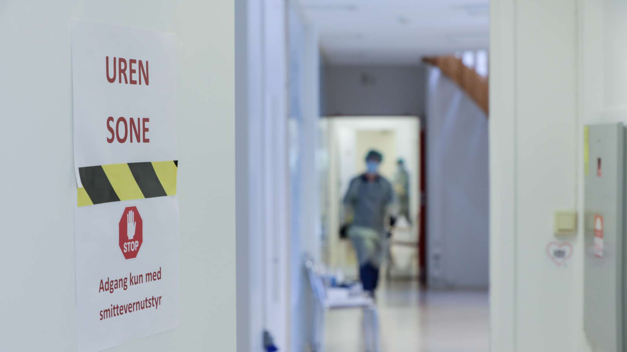 Helsearbeider i smittevernutstyr i en trappeoppgang, innenfor en dør med skiltet "Uren sone - adgang kun med smittevernutstyr"