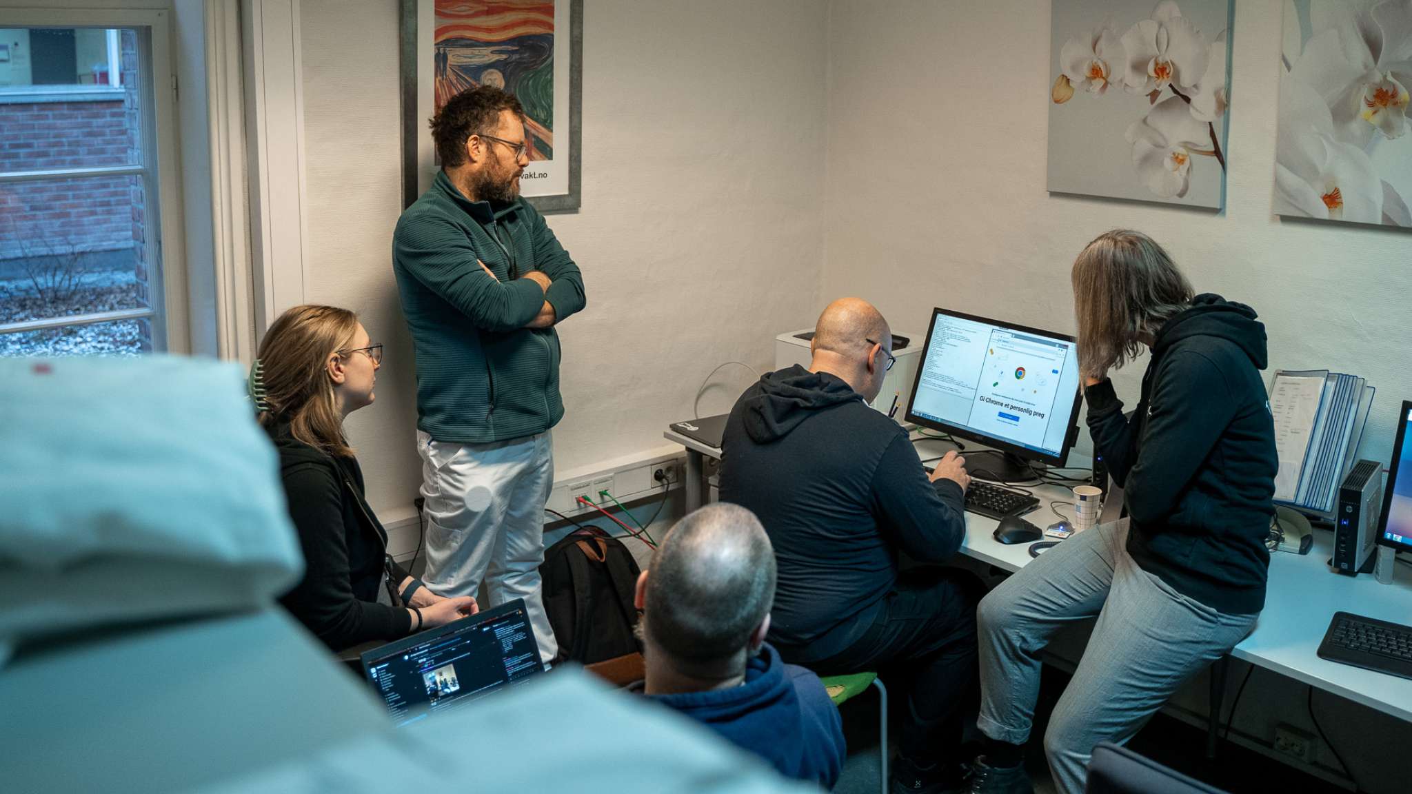 En lege ser på en gruppe utviklere som programmerer på en datamaskin. Foto.