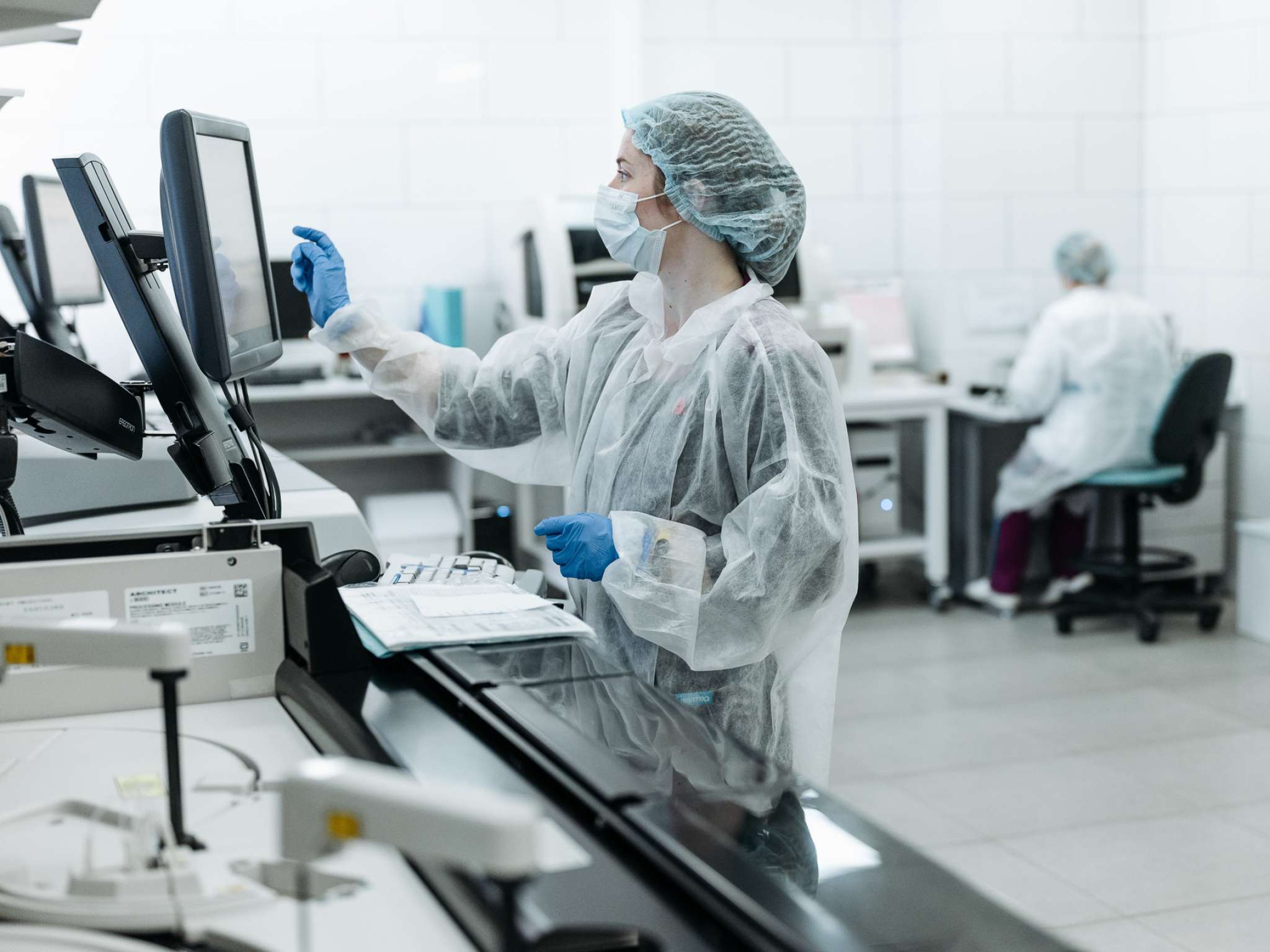Kvinne i smittevernklær trykker på en skjerm i et laboratorium. Foto.