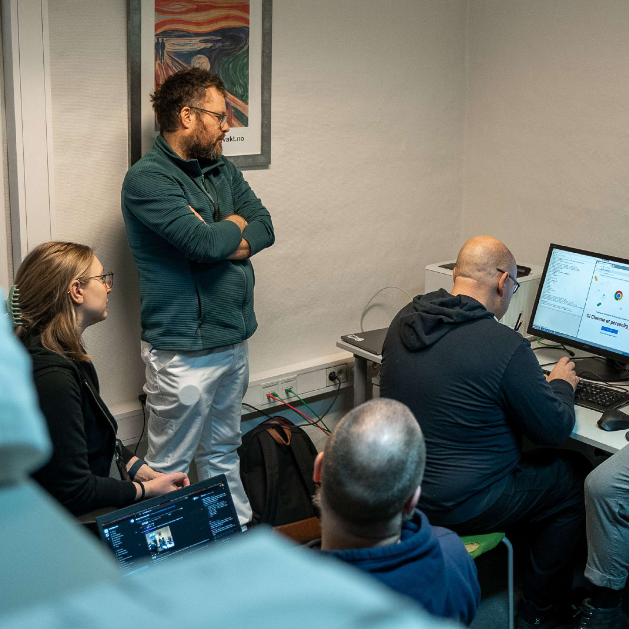 En lege ser på en gruppe utviklere som programmerer på en datamaskin. Foto.